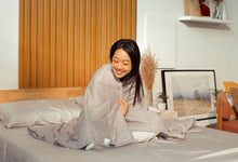 Happy woman hugging Sonno Huggy Blanket in a Japandi bedroom